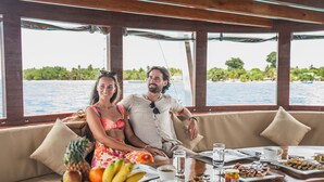 Una pareja en un bote, con una mesa dispuesta para el desayuno, que incluye frutas, pasteles y bebidas.