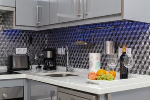 Una cocina moderna con encimera blanca, cafetera, una botella de vino y un frutero.