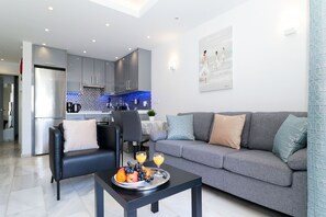 Una sala moderna con un sofá gris, un sillón negro y un comedor con una cocina al fondo.