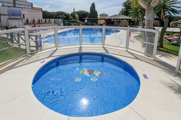 Una piscina redonda con borde de azulejos, rodeada por una valla blanca y vistas despejadas del entorno.