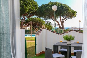 Un espacio al aire libre con mobiliario de mimbre y vistas a la piscina y a los árboles.
