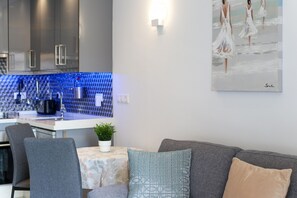 Une cuisine moderne avec un revêtement mural bleu, un coin repas avec une table et des chaises, et un canapé gris agrémenté de coussins décoratifs.
