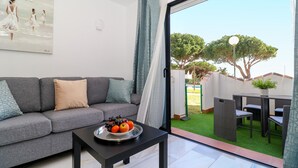 Una sala de estar moderna con un sofá gris, una mesa de centro negra con un frutero y un amplio ventanal con vistas a un jardín y árboles.