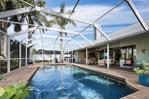A swimming pool with a glass enclosure, surrounded by outdoor furniture and palm trees. - Luxury Canal Home | Pool, Spa & Dock Near Beach (Nokomis)
