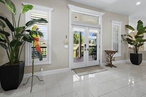 A clean, well-lit hallway with a tiled floor, a large potted plant, a decorative bird sculpture, and a door leading to an outdoor area. - Luxury Canal Home | Pool, Spa & Dock Near Beach (Nokomis)