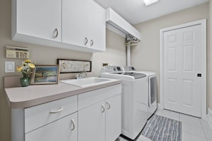 A laundry room with a washing machine, dryer, and a sink. There is a cabinet above the sink and a framed picture on the counter. - Luxury Canal Home | Pool, Spa & Dock Near Beach (Nokomis)