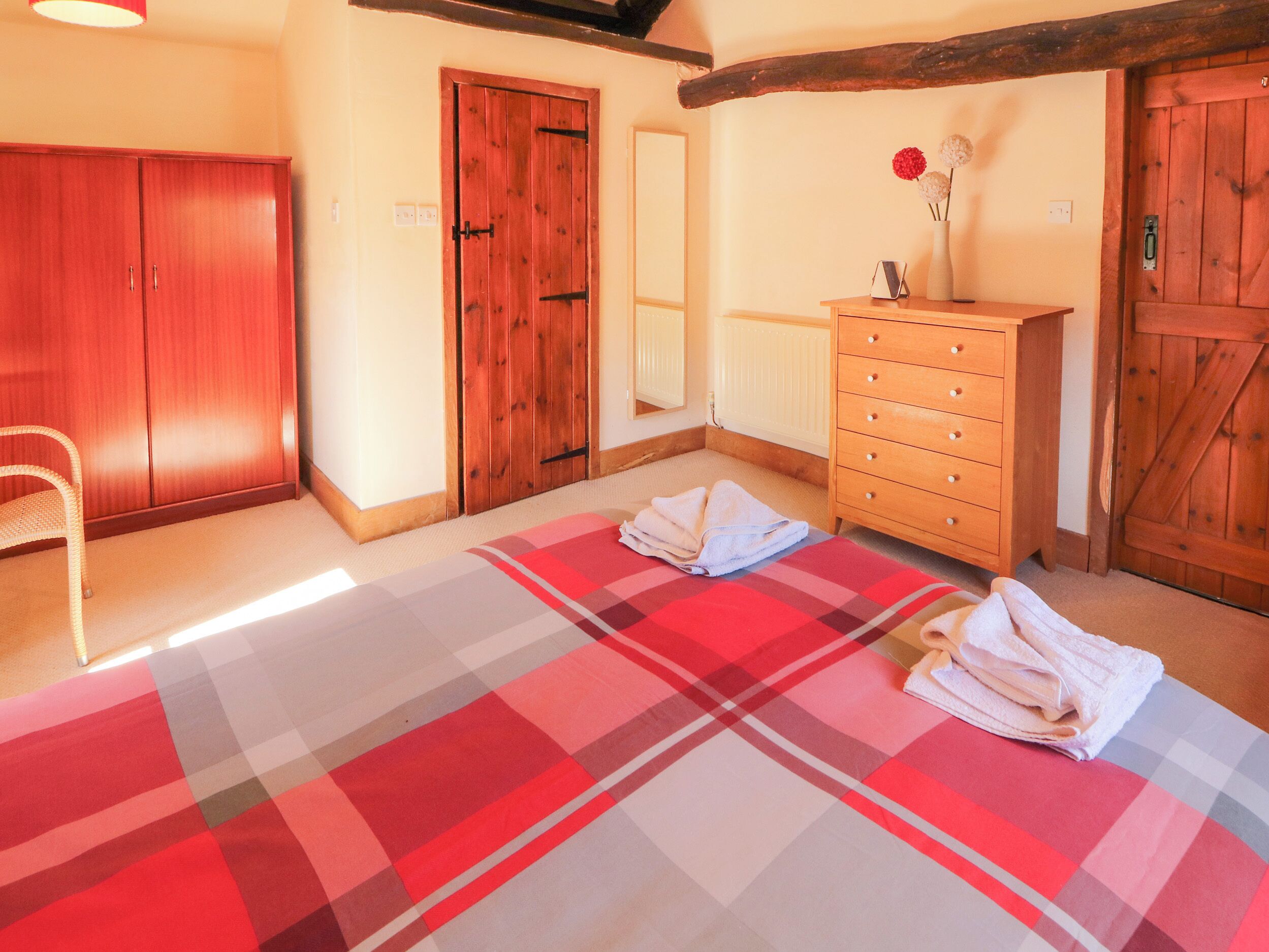 Ein Zimmer mit Schachbrettmuster-Teppich, Holzschrank und Kommode mit Blumenvase.