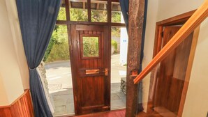 Une porte en bois avec une fenêtre, un paillasson rouge devant l’entrée et un escalier avec des rampes en bois.