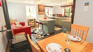 Un salon chaleureux avec un canapé rouge, une table à manger dressée pour deux personnes et un poêle à bois.