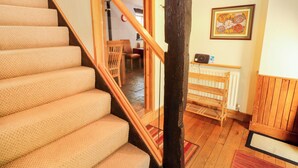 Un escalier dont les marches sont recouvertes d’une moquette beige et qui possède des rampes en bois, menant à une pièce dotée d’un plancher en bois, d’un radiateur et d’un tableau encadré accroché au mur.