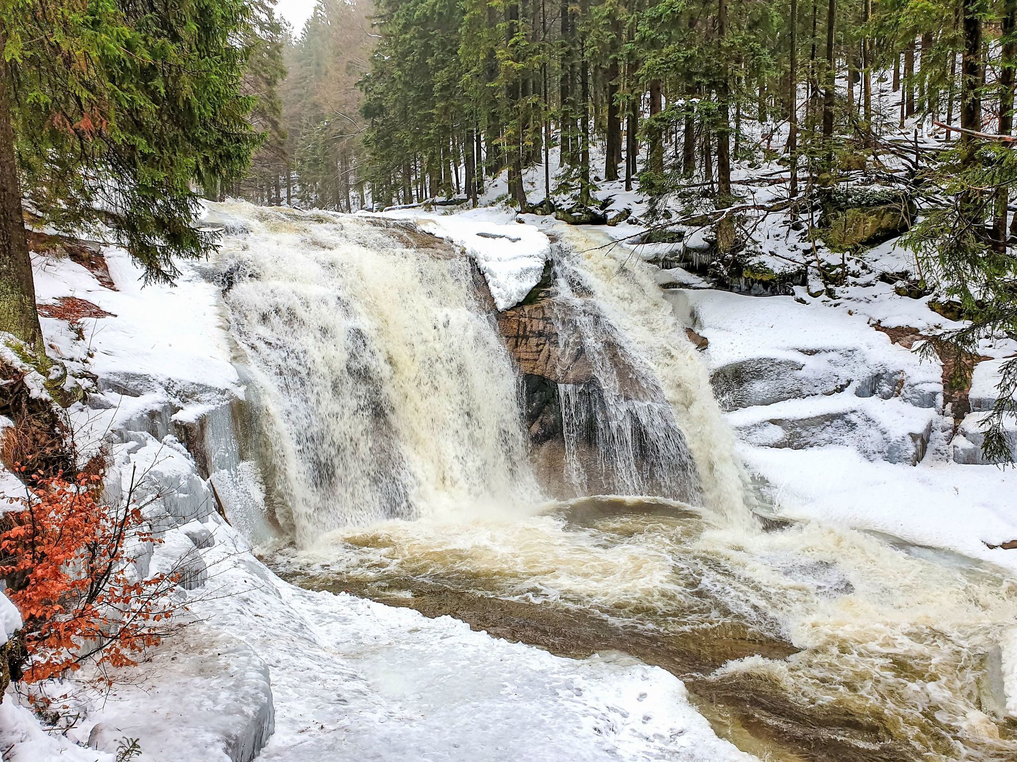 A waterfall in a forested area with snow-covered ground and trees.