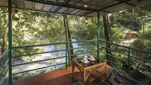 Una habitación con vistas a un río, una mesa con sillas y una estructura de techo de paja al fondo.