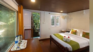 Habitación de hotel con cama, una mesa con alimentos para el desayuno, un ventilador y vistas a zonas verdes.
