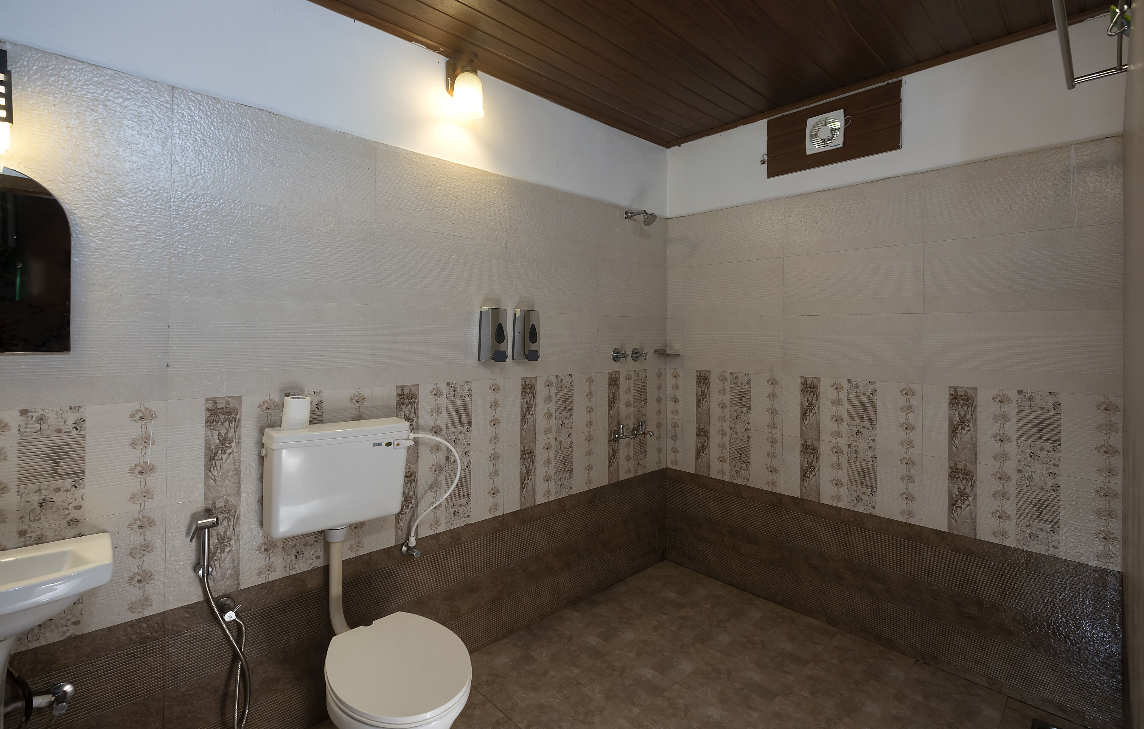 Et badeværelse med toilet, vask, bruser og en håndtørrer på væggen.