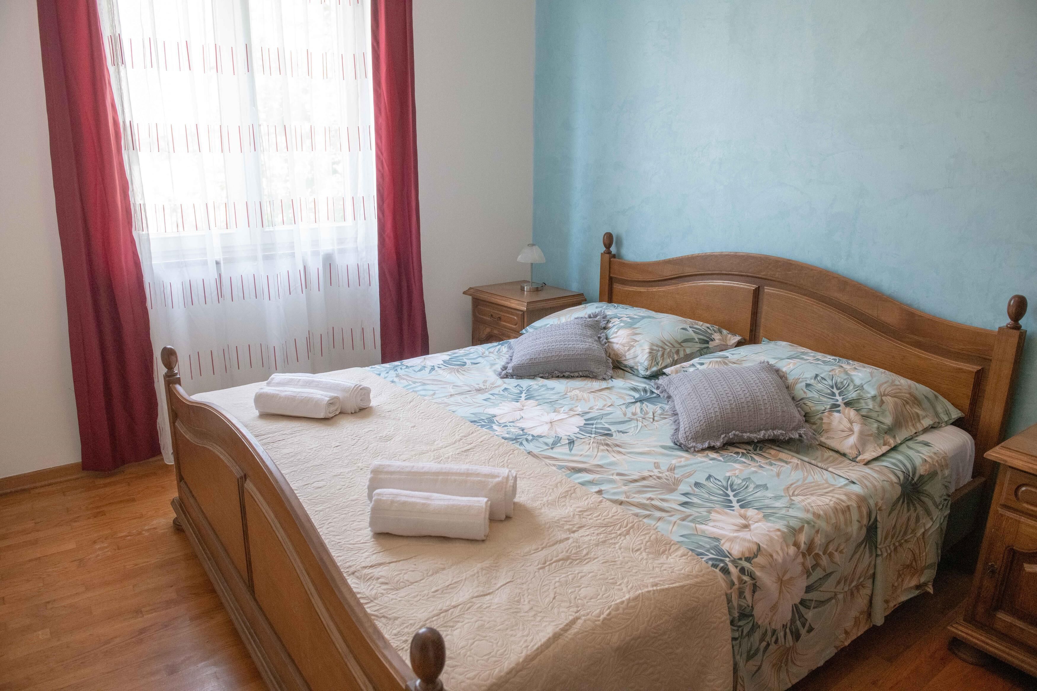A neatly made bed with a floral bedspread, two pillows, and two folded towels.