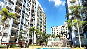 Piscina rodeada por edifícios residenciais altos com varandas, céu claro e palmeiras.