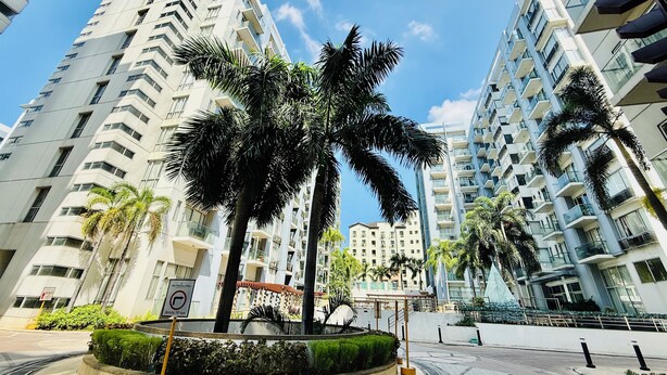 Uma praça urbana moderna com edifícios altos, palmeiras e uma área pedonal circular.