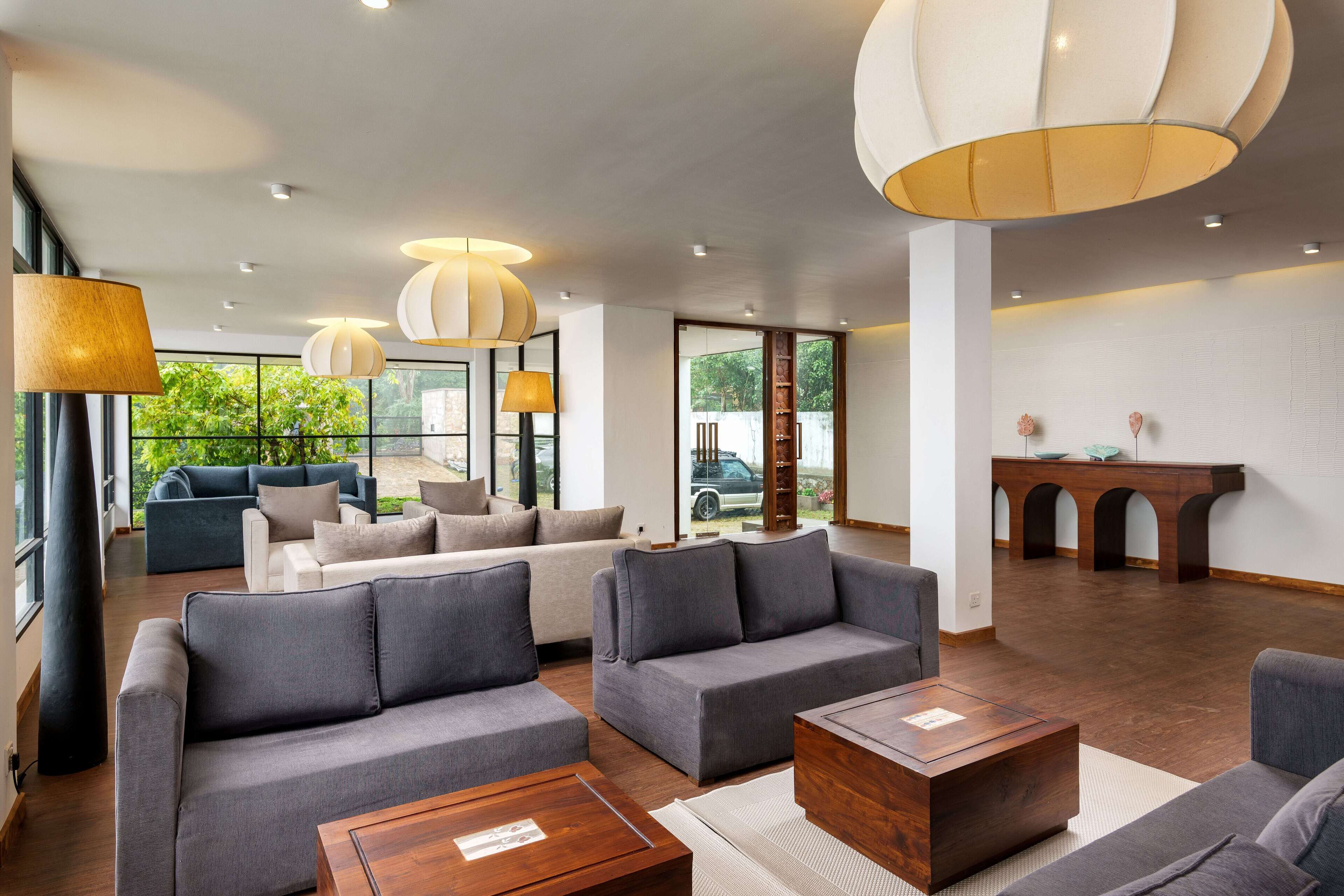 A spacious lobby with grey sofas, wooden coffee tables, and pendant lighting.