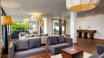 A spacious lobby with grey sofas, wooden coffee tables, and pendant lighting.