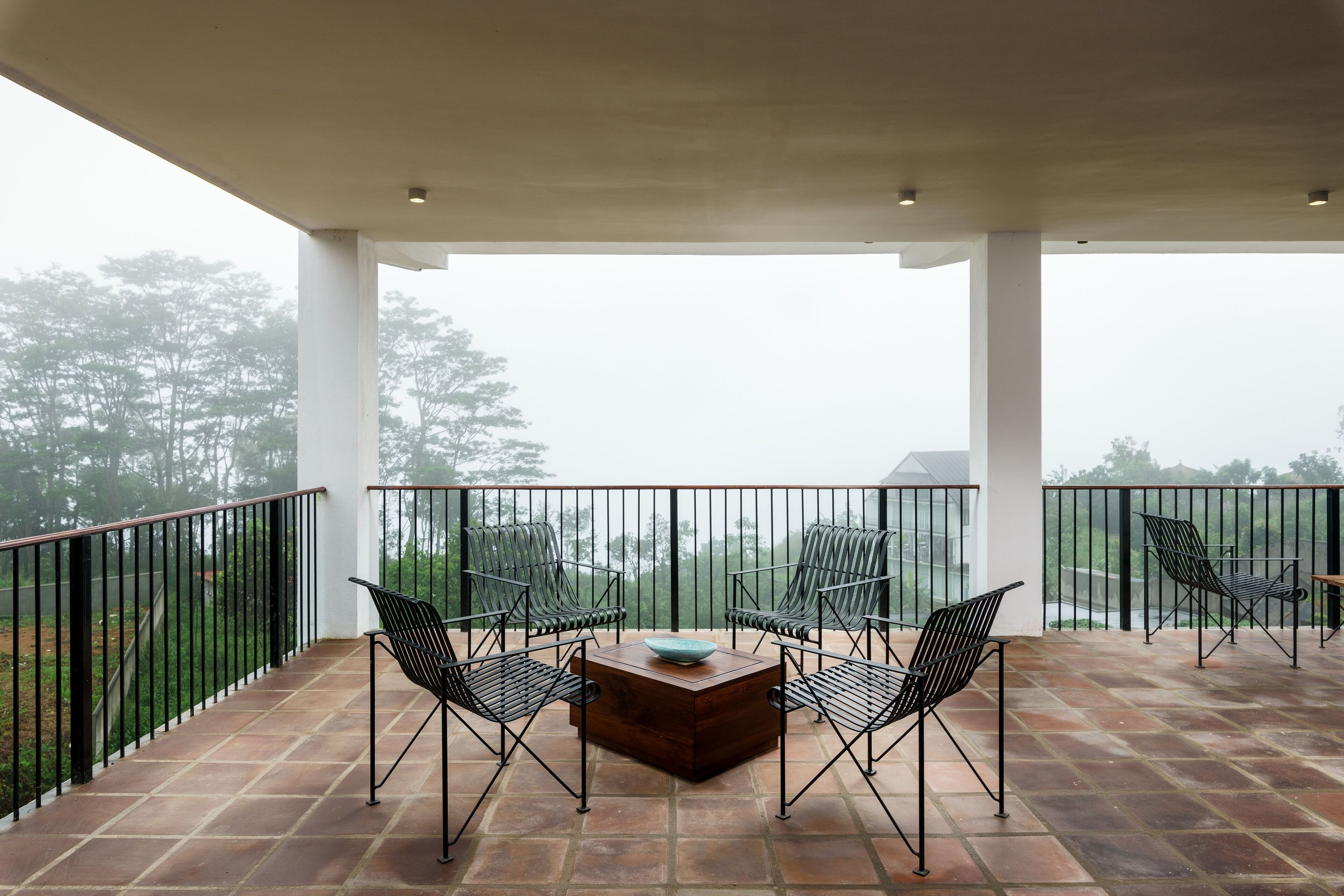 Un patio techado al aire libre con una mesa y cuatro sillas, rodeado por una barandilla de metal negro.