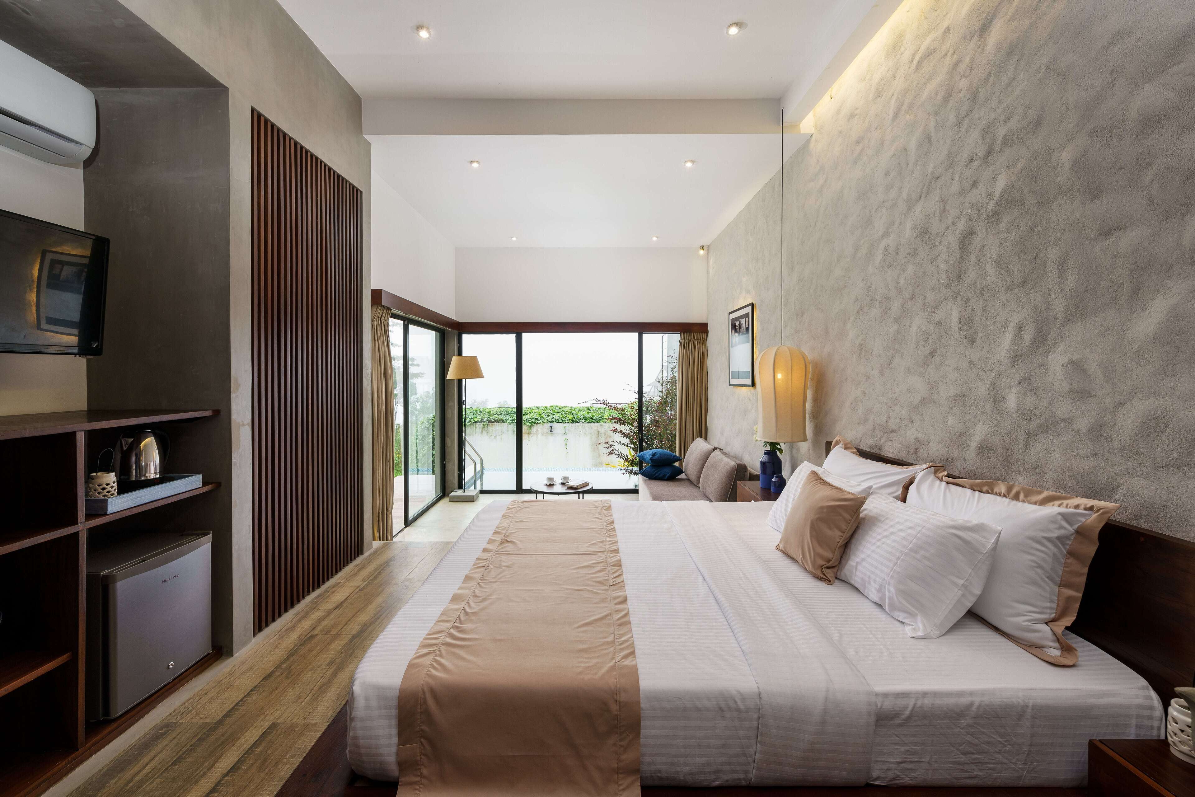 A modern hotel room with a large bed, a TV mounted on the wall, and a view of the outdoors.