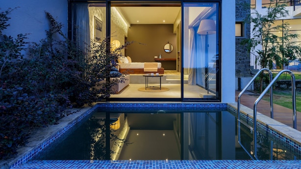 A modern hotel room with a glass door leading to a bedroom, a small pool, and a staircase.
