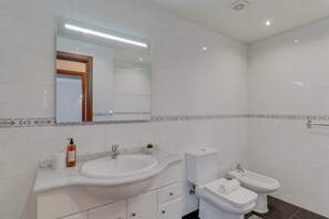 A modern bathroom with a large sink, toilet, and bidet, white tiles, and a mirror with a wooden frame. - Tropical Pearl by Atlantic Holiday (Funchal)