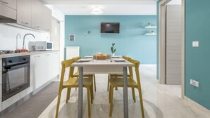 A compact kitchen with modern appliances, a dining area with yellow chairs, and teal walls. - Sicilia by Interhome (Balestrate)