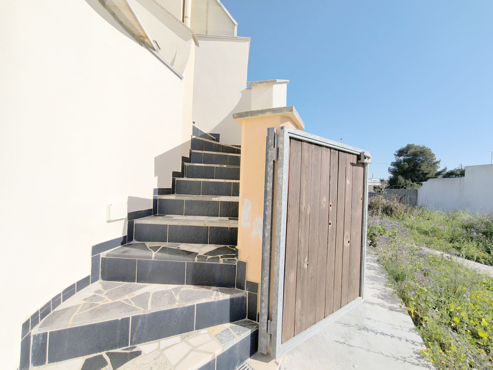 A set of outdoor stairs leading to a wooden gate, with a clear sky above.