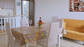 Un coin repas avec une table dressée pour quatre personnes, des chaises blanches, une nappe à motifs floraux et un vase rempli de fleurs.