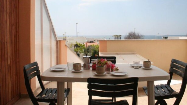 Une table à manger dressée pour deux personnes sur un balcon avec vue sur la mer.