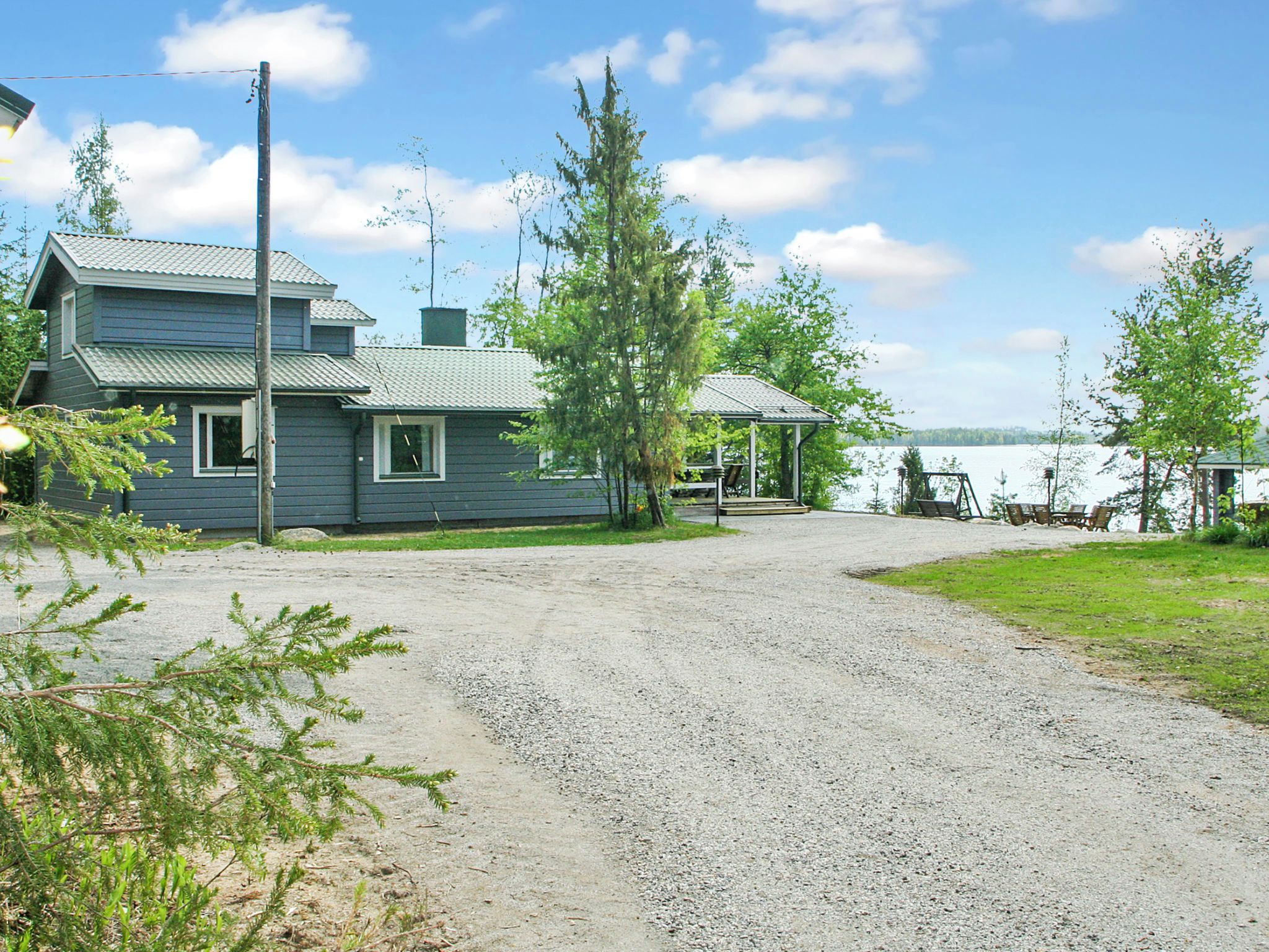 Une maison à deux étages avec une allée de gravier menant à un quai au bord d’un lac.