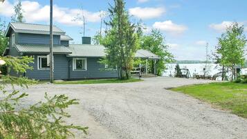Une maison à deux étages avec une allée de gravier menant à un quai au bord d’un lac.