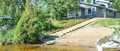A house with a dock and a boat, surrounded by trees and a clear stream.