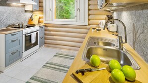 A modern kitchen with wooden log walls, a stove, sink, and a window overlooking greenery. - Ilotupa by Interhome (Pertunmaa)