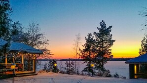 A snow-covered landscape with a wooden cabin and a gazebo, both featuring outdoor seating and string lights. - Ilotupa by Interhome (Pertunmaa)