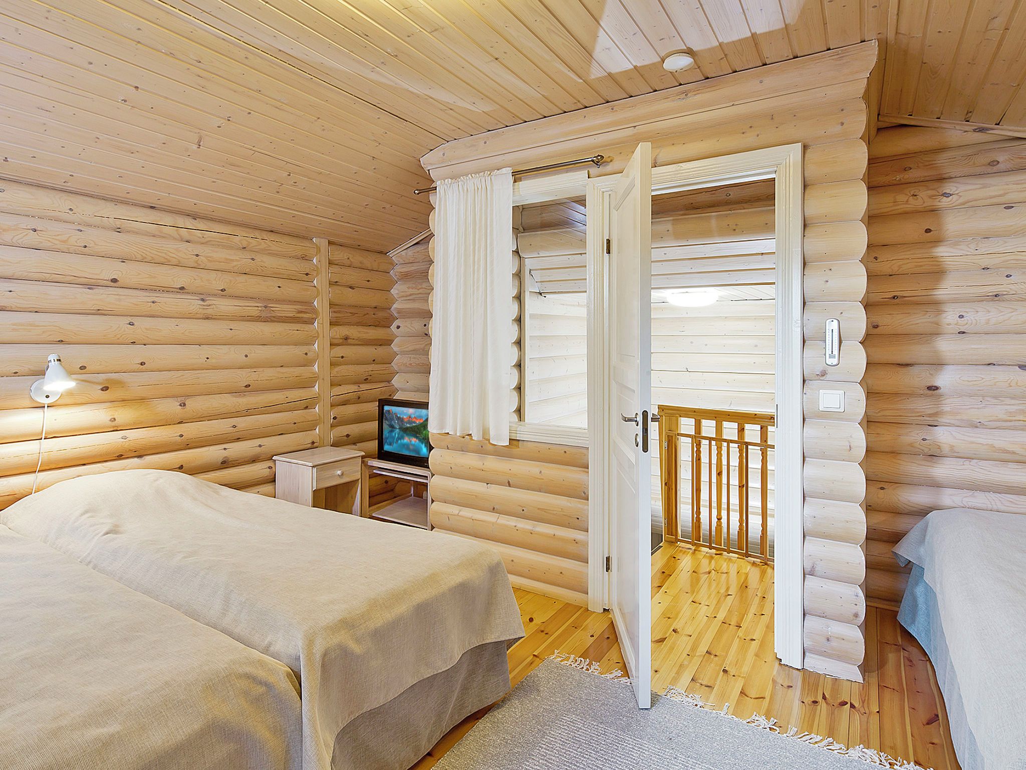 Een slaapkamer in een blokhut met een bed, een televisie en een houten deur die uitkomt op een balkon.