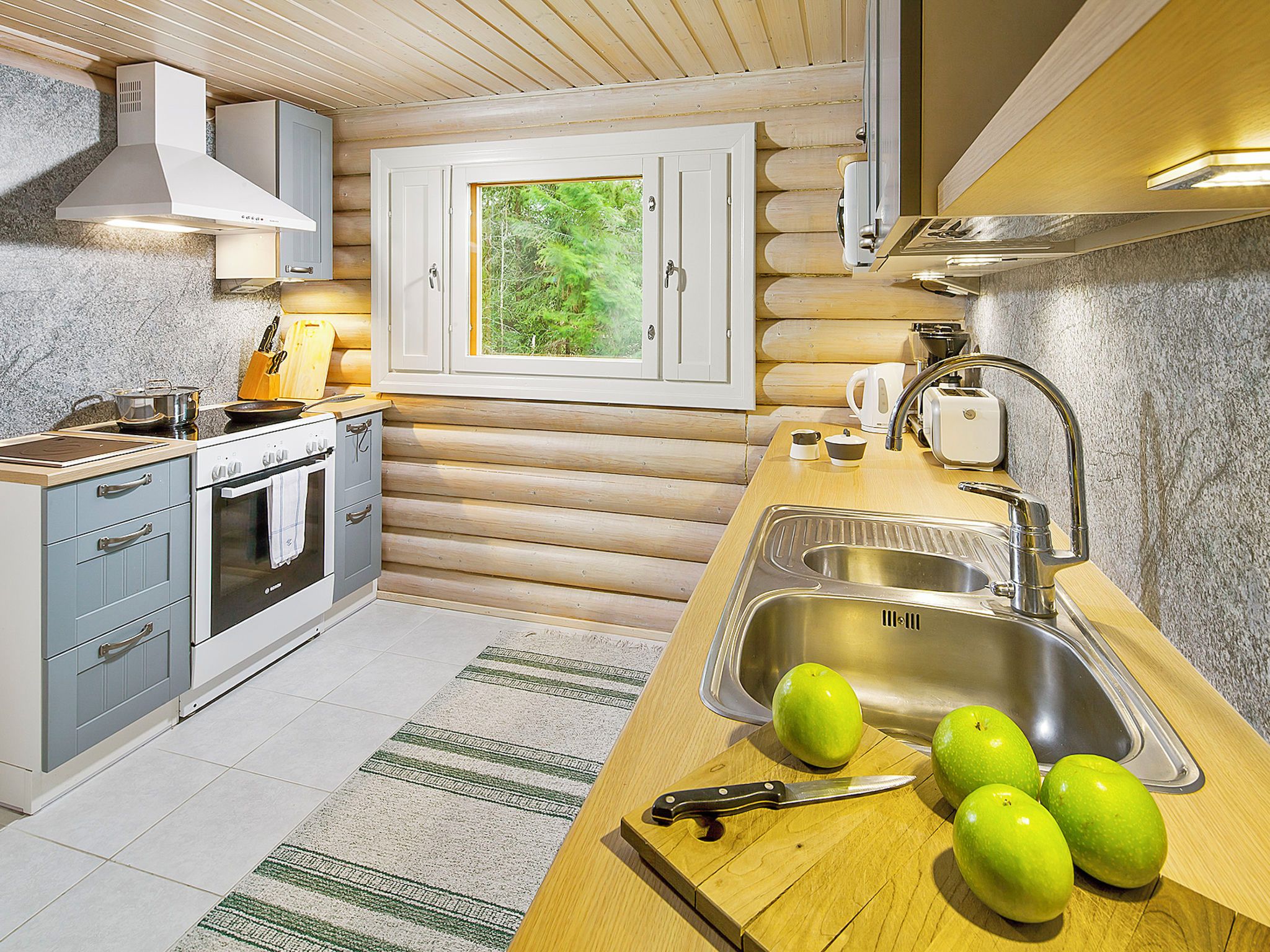 Une cuisine moderne avec un intérieur en bois, un four encastré, un évier et une fenêtre donnant sur un espace verdoyant.