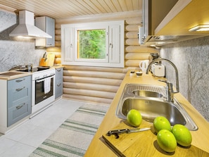 A modern kitchen with a wooden interior, a built-in oven, a sink, and a window overlooking greenery. - Ilotupa by Interhome (Pertunmaa)