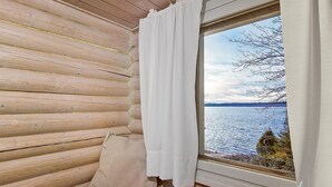 A cozy cabin room with a wooden interior, a window with a view of a lake, and a cushion on the floor. - Ilotupa by Interhome (Pertunmaa)