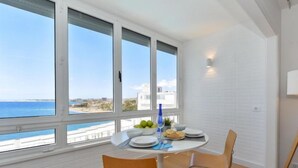 A dining area with a view of the sea, white tiled walls, and a table set with plates and a vase. - Apartment Balcon by Interhome (San Agustín)