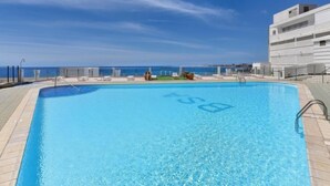 A clear blue swimming pool with a view of the sea and a modern building in the background. - Apartment Balcon by Interhome (San Agustín)