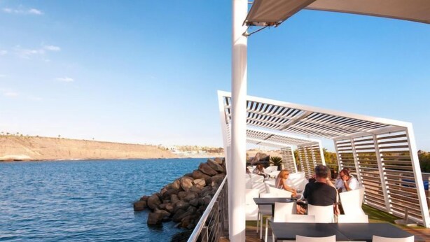 A deck with outdoor seating overlooking a body of water, featuring a rocky shoreline in the background. - Cabosos 4 by Interhome (Maspalomas)