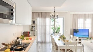 A modern kitchen with white cabinets, a dining area with a white table and chairs, a TV, and a view of the outdoors through large windows. - Cabosos 4 by Interhome (Maspalomas)