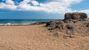A sandy beach with a rocky outcrop and the ocean in the background. - Papagayo San Agustin by Interhome (Maspalomas)