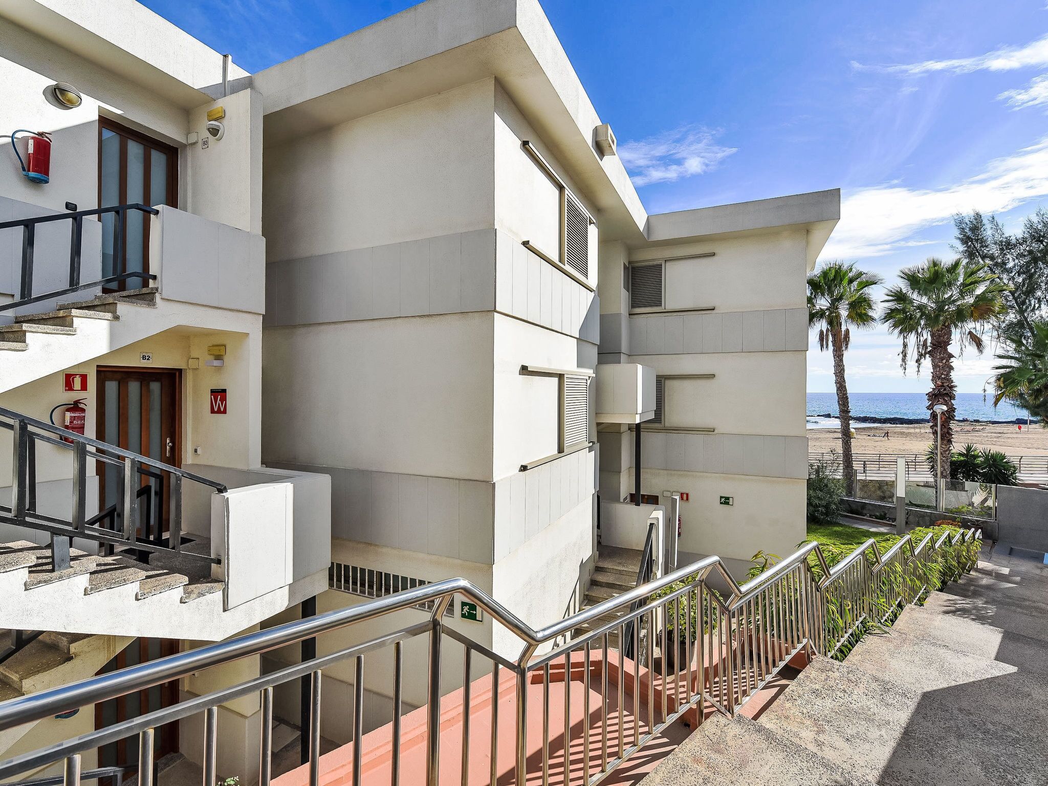 A modern building with a staircase leading to a balcony overlooking a beach.