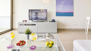 A modern living room with a flat-screen TV, a painting, and a glass table with drinks and fruit. - Papagayo San Agustin by Interhome (Maspalomas)