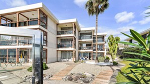 A modern multi-story building with balconies, a palm tree, and a garden with a pathway. - Papagayo San Agustin by Interhome (Maspalomas)