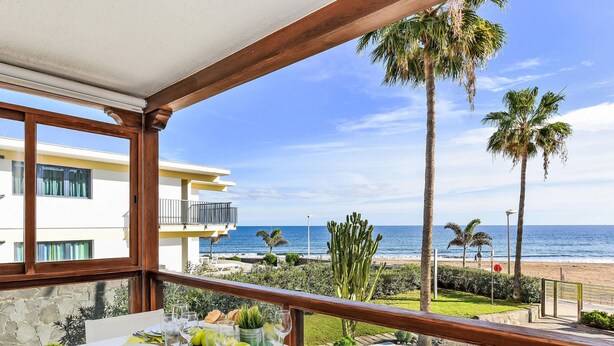 A balcony with a table set for dining, overlooking a beach and ocean. - Papagayo San Agustin by Interhome (Maspalomas)