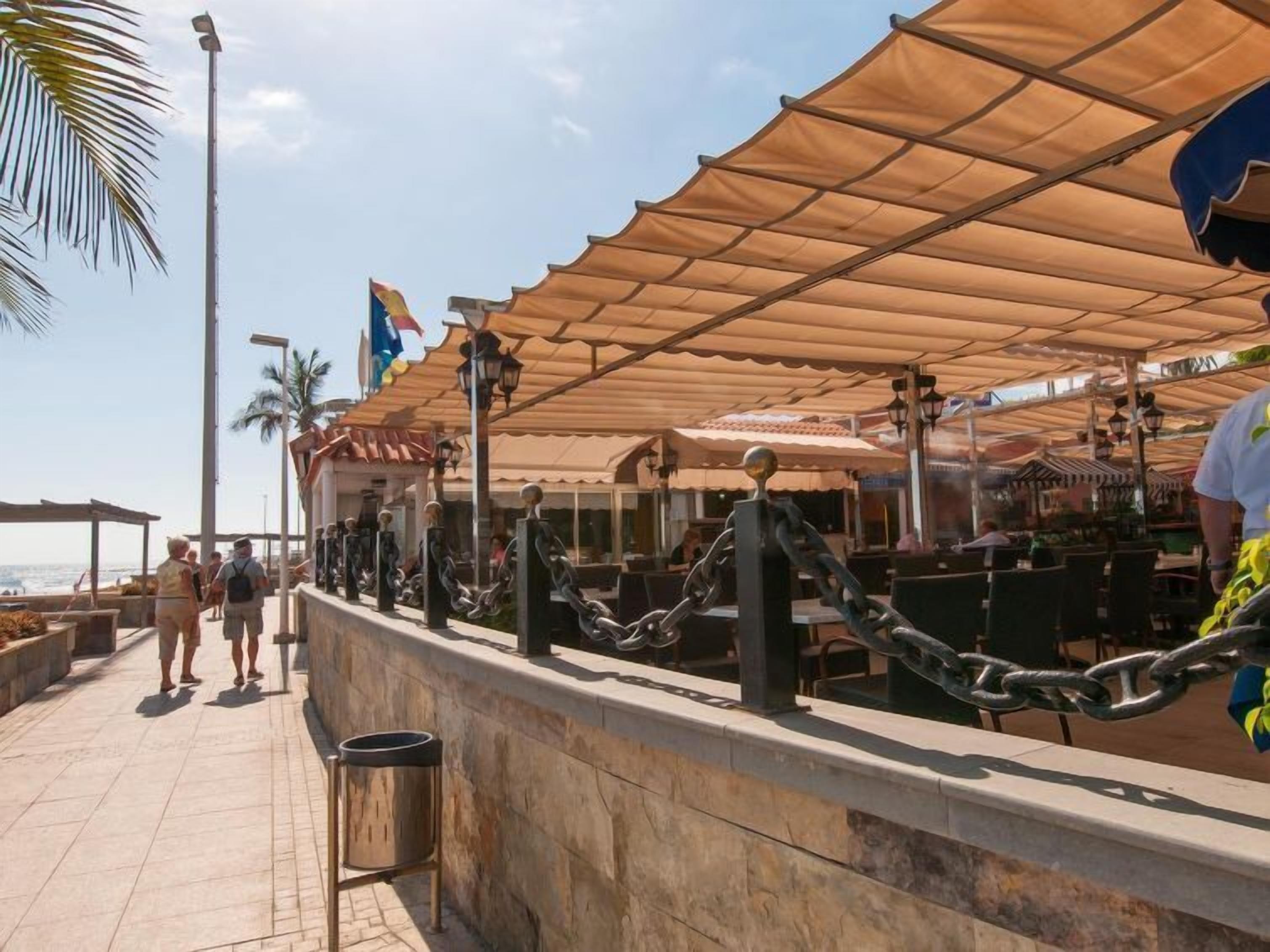 An outdoor dining area with chain-link barriers, tables, and umbrellas.